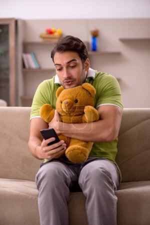 Foto de Joven estudiante masculino con oso de juguete en casa - Imagen libre de derechos