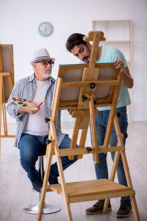 Photo for Old male painter teaching young male student at studio - Royalty Free Image