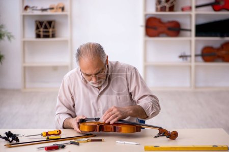 Téléchargez les photos : Ancien réparateur réparant des instruments de musique à l'atelier - en image libre de droit