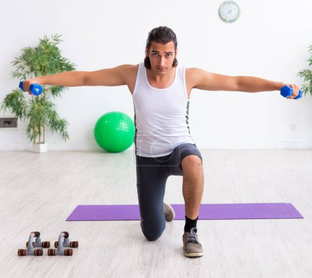 Photo for The young handsome man doing sport exercises indoors - Royalty Free Image