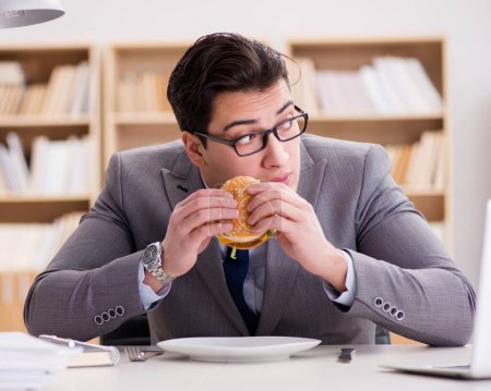 Foto de El hambriento empresario divertido comiendo sándwich de comida chatarra - Imagen libre de derechos