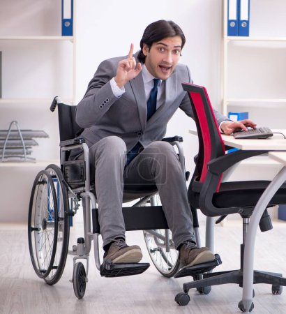 Foto de El joven empleado guapo en silla de ruedas que trabaja en la oficina - Imagen libre de derechos
