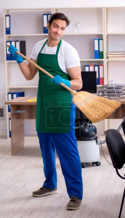 Foto de El joven contratista guapo limpiando la oficina - Imagen libre de derechos