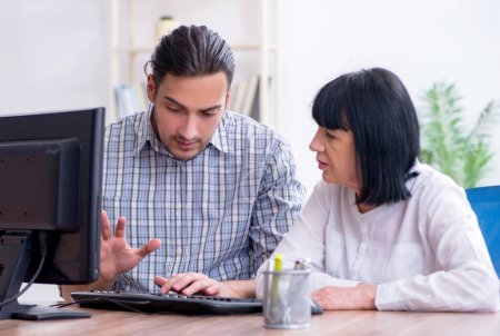 Foto de Joven empleado masculino explicando a una vieja colega cómo usar la computadora - Imagen libre de derechos