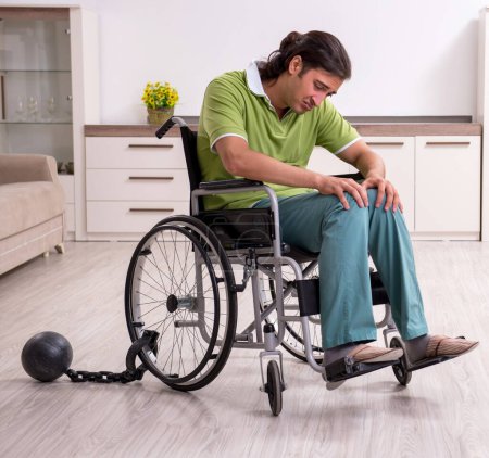 Téléchargez les photos : Le jeune homme invalide en fauteuil roulant souffrant à la maison - en image libre de droit