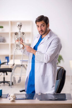 Foto de Joven médico masculino estudiando esqueleto humano en la clínica - Imagen libre de derechos