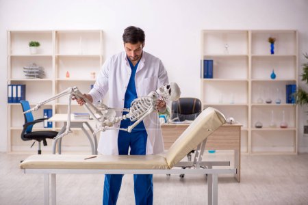 Photo for Young male doctor with skeleton at the hospital - Royalty Free Image