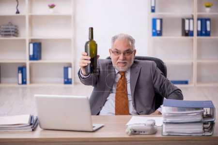 Téléchargez les photos : Vieil employé buvant de l'alcool sur le lieu de travail - en image libre de droit