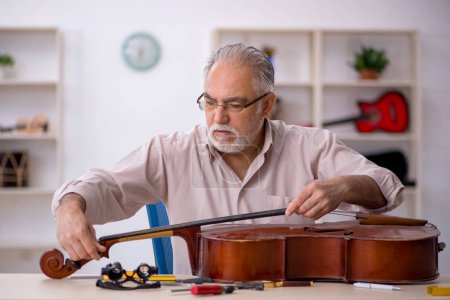Téléchargez les photos : Ancien réparateur réparant des instruments de musique à l'atelier - en image libre de droit
