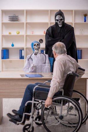 Téléchargez les photos : Vieux patient masculin en fauteuil roulant visitant deux médecins du diable - en image libre de droit