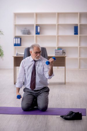 Photo for Old employee doing sport exercises during break - Royalty Free Image