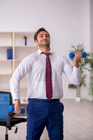 Photo for Young employee doing sport exercises during break - Royalty Free Image
