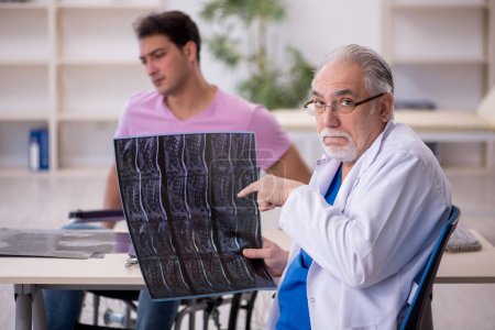 Téléchargez les photos : Jeune homme en fauteuil roulant visitant vieux médecin radiologue - en image libre de droit