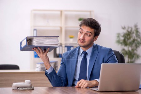 Photo for Young male employee and too much work at workplace - Royalty Free Image