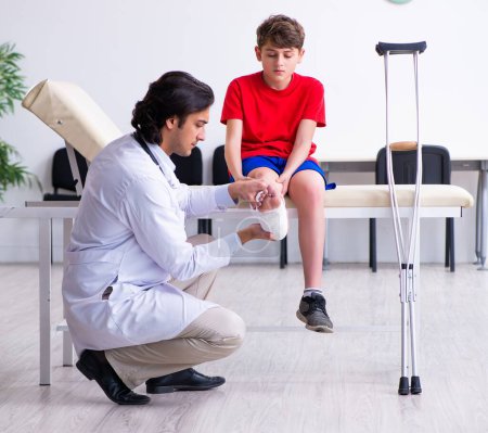 Foto de El niño lesionado pierna visitando al joven médico traumatólogo - Imagen libre de derechos
