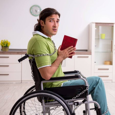 Téléchargez les photos : Le jeune homme invalide en fauteuil roulant souffrant à la maison - en image libre de droit