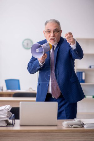 Téléchargez les photos : Old employee holding megaphone in the office - en image libre de droit