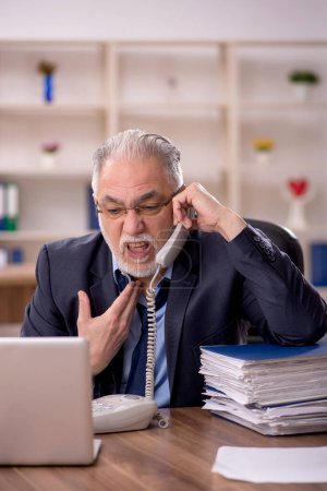 Téléchargez les photos : Vieil homme d'affaires employé mécontent du travail excessif dans le bureau - en image libre de droit