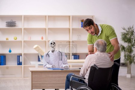 Foto de Viejo paciente masculino en silla de ruedas visitando esqueleto médico - Imagen libre de derechos