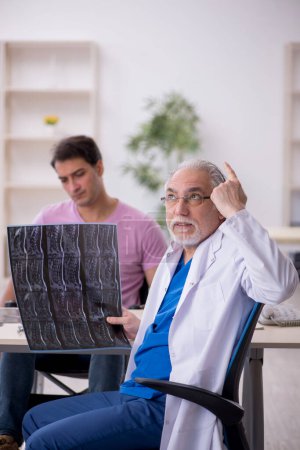 Photo for Young man in wheelchair visiting old male doctor radiologist - Royalty Free Image
