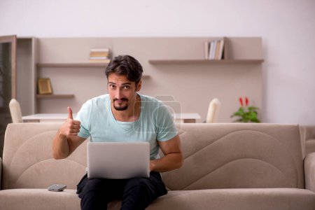 Photo for Young male student sitting on the sofa with computer at home - Royalty Free Image