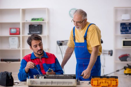 Photo for Two repairmen repairing air-conditioner at workshop - Royalty Free Image