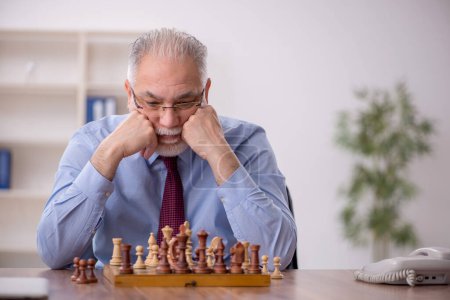 Photo for Old male employee playing chess in the office - Royalty Free Image