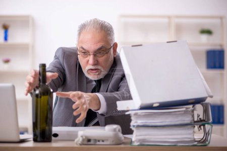 Foto de Viejo empleado bebiendo alcohol en el lugar de trabajo - Imagen libre de derechos
