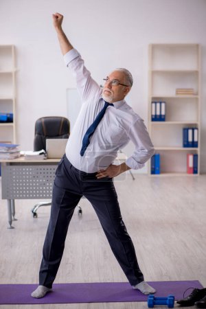 Photo for Old male employee doing sport exercises during break - Royalty Free Image