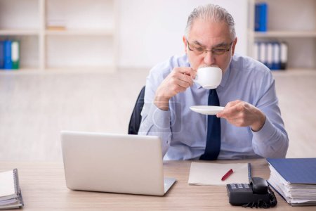 Foto de Old employee drinking tea at workplace - Imagen libre de derechos