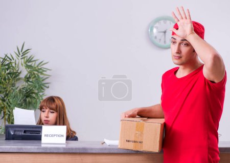 Photo for The young male courier delivering box to hotels reception - Royalty Free Image