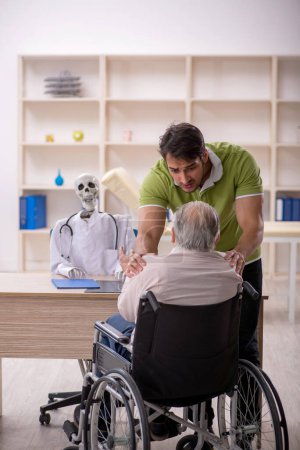 Photo for Old male patient in wheel-chair visiting skeleton doctor - Royalty Free Image