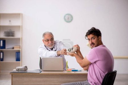 Téléchargez les photos : Jeune patient visitant vieux médecin masculin dans le concept de rémunération - en image libre de droit