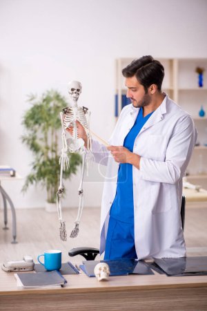 Téléchargez les photos : Jeune homme médecin étudiant le squelette humain à la clinique - en image libre de droit