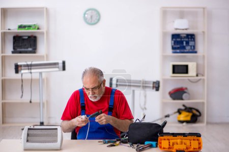 Foto de Viejo reparador masculino reparando calentador en el taller - Imagen libre de derechos