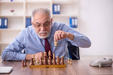 Photo for Old male employee playing chess in the office - Royalty Free Image