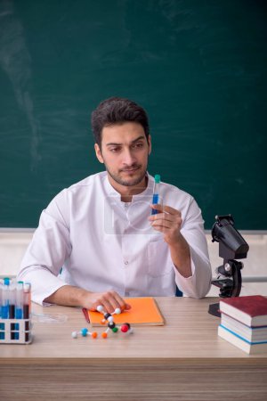 Téléchargez les photos : Jeune professeur de chimiste assis dans la salle de classe - en image libre de droit