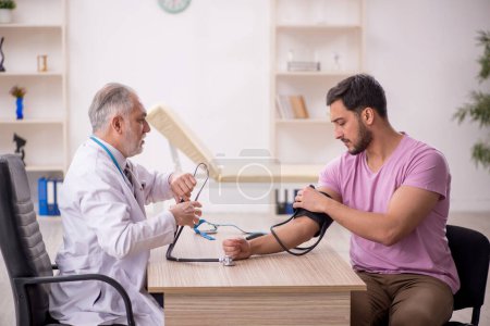 Foto de Médico viejo midiendo pacientes jóvenes presión arterial - Imagen libre de derechos