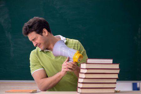 Téléchargez les photos : Young male student holding megaphone in classroom - en image libre de droit