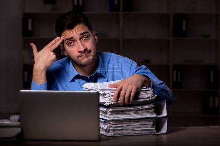 Téléchargez les photos : Young employee working late at workplace - en image libre de droit