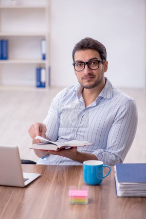Téléchargez les photos : Young businessman employee reading book at workplace - en image libre de droit