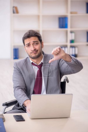 Téléchargez les photos : Young male employee in wheel-chair working at workplace - en image libre de droit