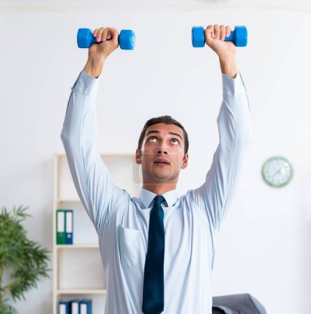Photo for The young handsome employee doing sport exercises at workplace - Royalty Free Image