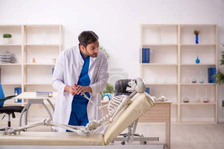Téléchargez les photos : Jeune homme médecin avec squelette à l'hôpital - en image libre de droit