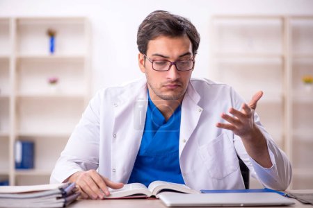 Photo for Young male doctor student reading book at the hospital - Royalty Free Image
