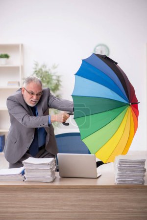 Téléchargez les photos : Old employee holding an umbrella at workplace - en image libre de droit