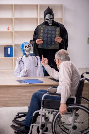 Foto de Viejo paciente masculino en silla de ruedas visitando a dos doctores diabólicos - Imagen libre de derechos