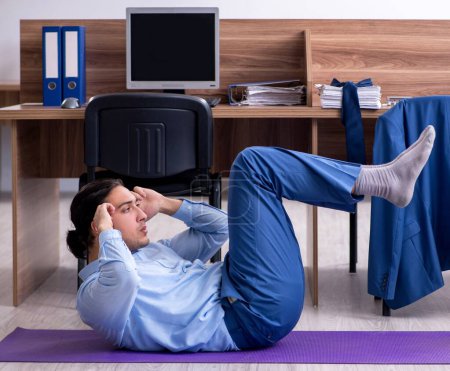 Photo for The young handsome businessman doing exercises at workplace - Royalty Free Image