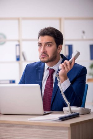 Photo for Young businessman employee speaking by phone at workplace - Royalty Free Image