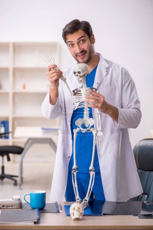 Téléchargez les photos : Jeune homme médecin étudiant le squelette humain à la clinique - en image libre de droit
